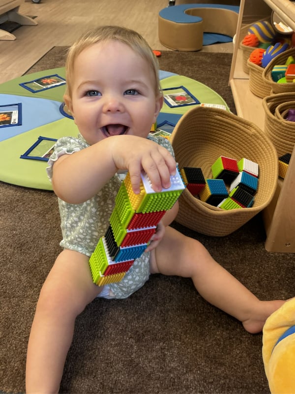 Smiling infant builds with colorful textured blocks during a hands-on learning activity at Primrose School of Forest Hill.