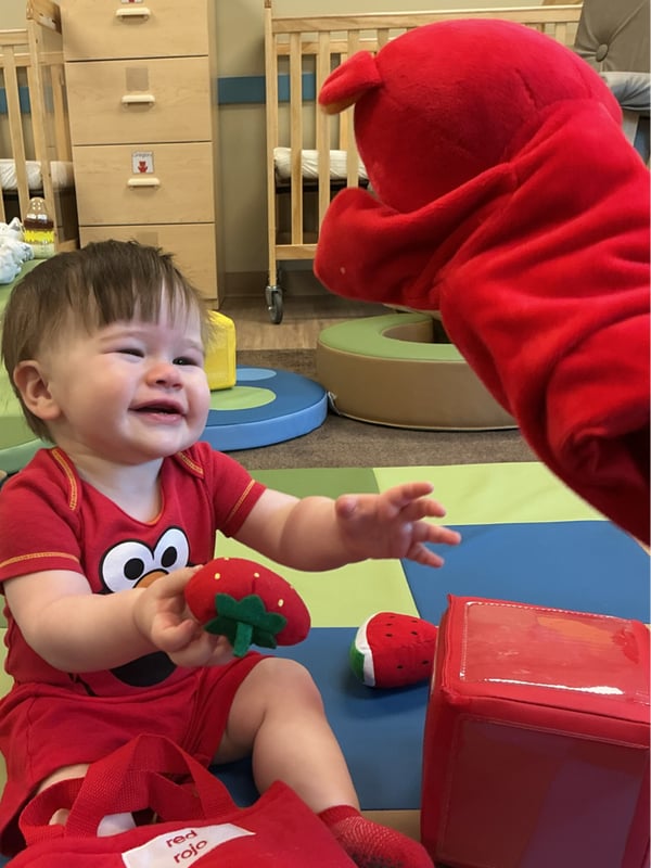 Infant at Primrose School of Forest Hill smiling and interacting with Benjamin the Bear, the Primrose Friend, during a fun classroom learning experience.