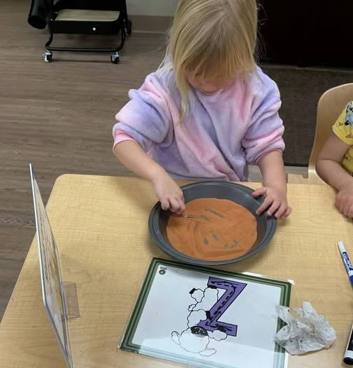 Preschooler tracing the letter Z in a sensory activity that encourages letter recognition, tactile learning, and early literacy skills at Primrose School.