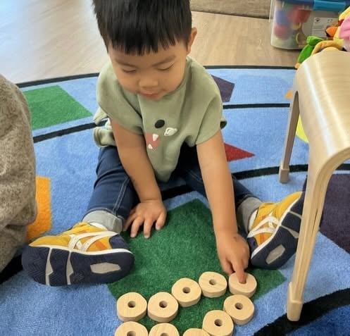 Toddler arranging wooden counting discs during a hands-on math activity that develops number recognition, problem-solving, and fine motor skills at Primrose School.