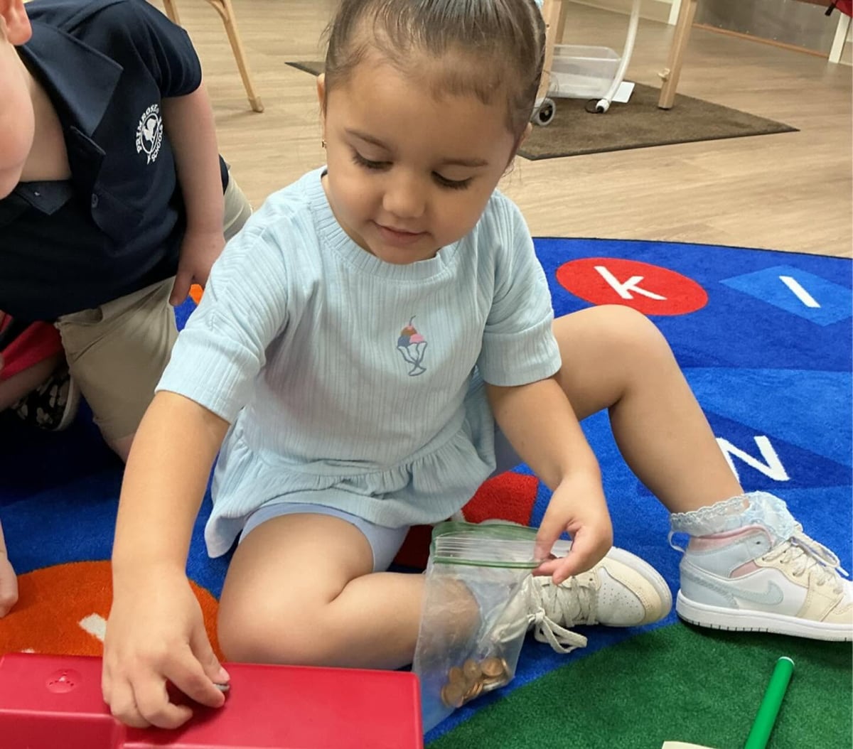 Preschooler using pennies during a hands-on math activity to practice counting, number recognition, and problem-solving skills at Primrose School.