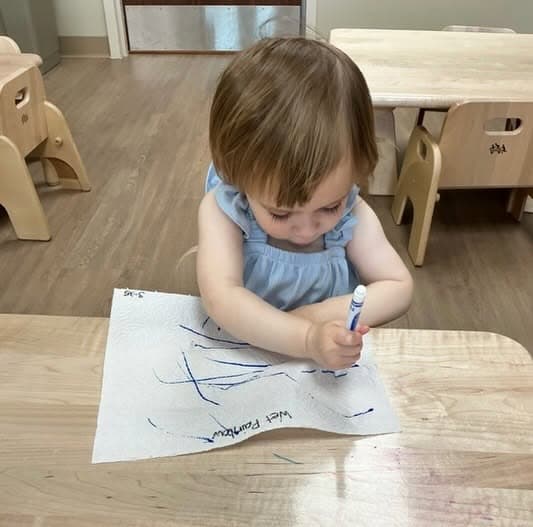 Toddler practicing early writing and fine motor skills by drawing with a marker during a hands-on learning activity at Primrose School.