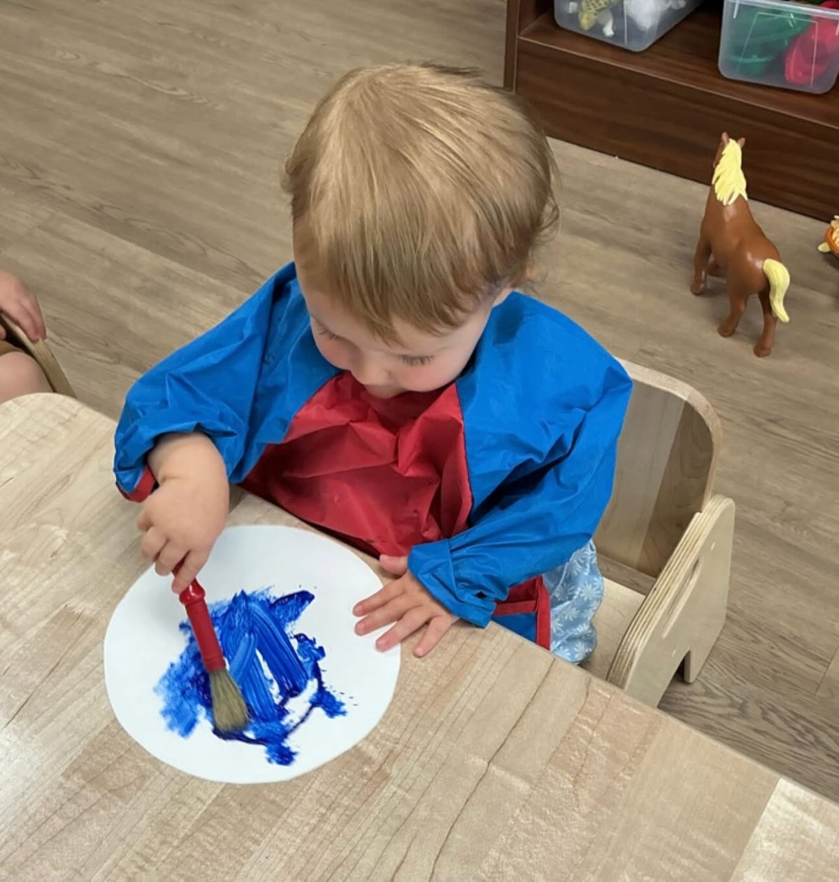 Toddler painting with a brush during a creative art activity that encourages self-expression, sensory exploration, and fine motor development at Primrose School.
