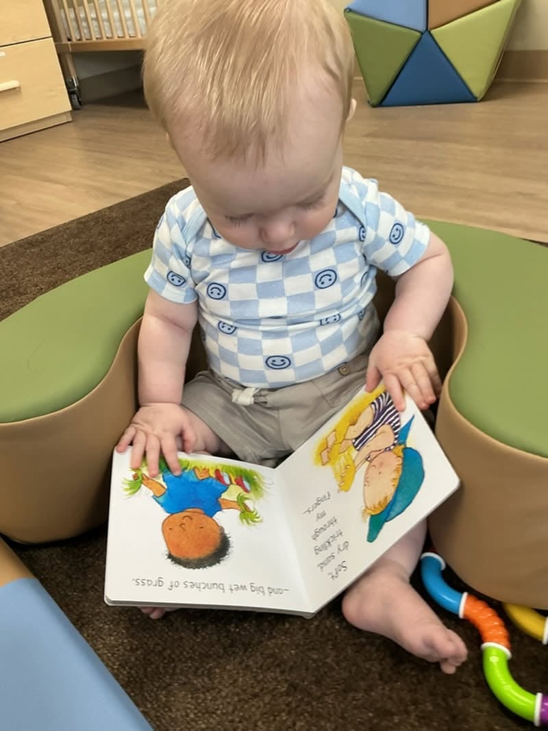 Infant exploring a colorful board book during story time, supporting early language development, visual tracking, and a lifelong love of reading at Primrose School.