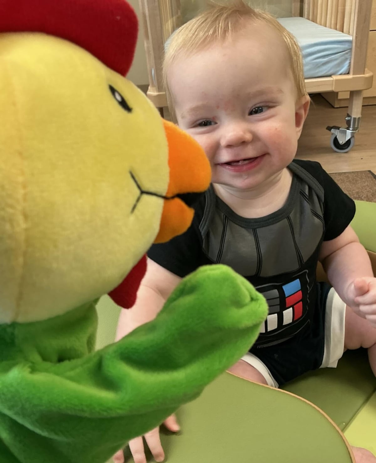 Infant smiling and interacting with a classroom puppet during a playful activity that encourages social-emotional development, communication, and engagement at Primrose School.