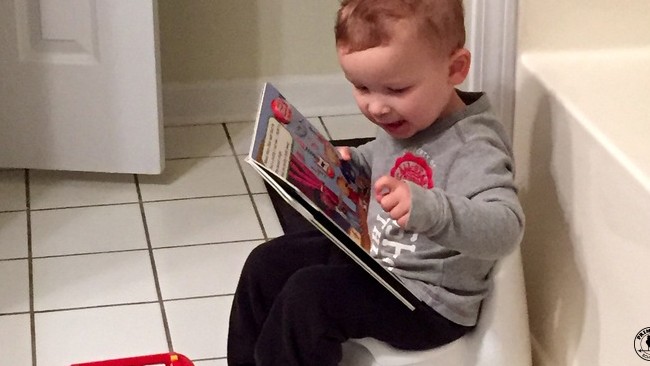 A little boy sitting on a potty in the bathroom, excitedly reading a storybook