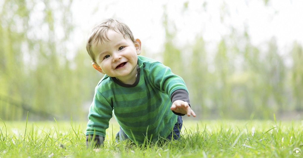A smiling baby boy crawls outdoors on grass