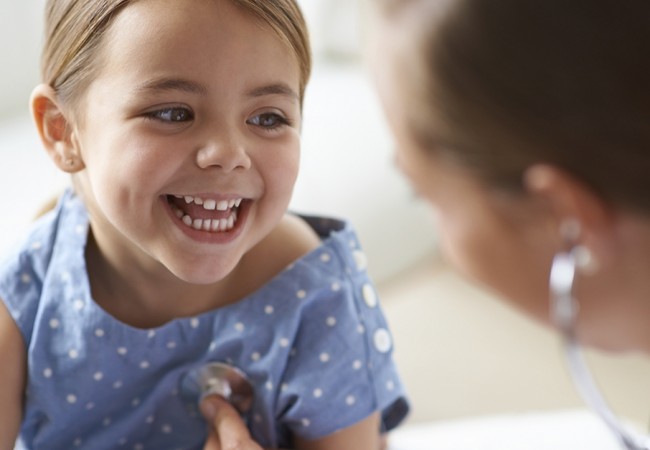 Little girl smiling as the doctor checks her heart beat with a stethoscope