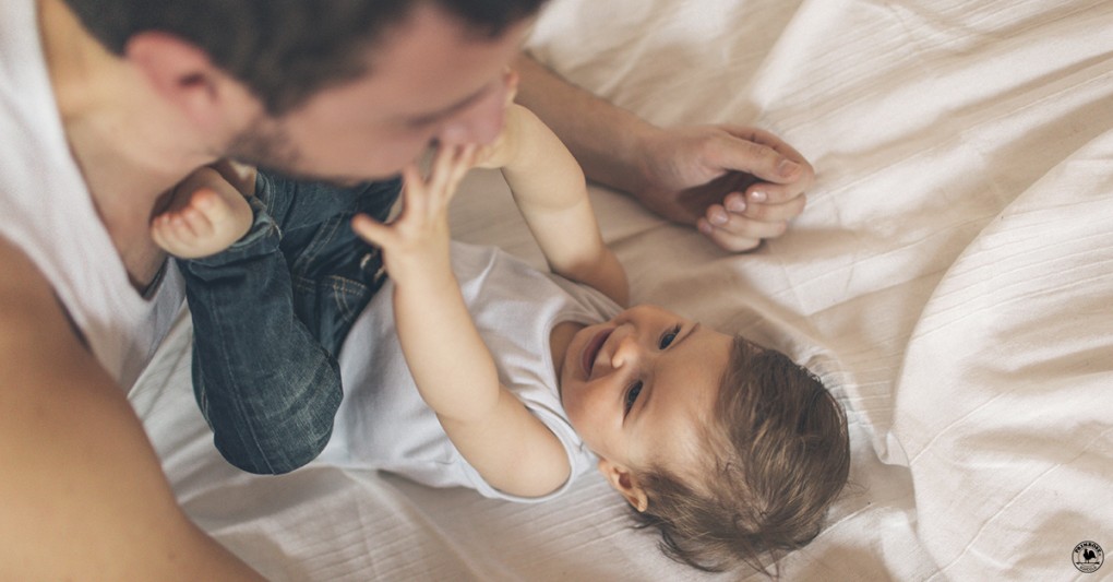 Toddler playfully reaches out to his father while they play on the bed