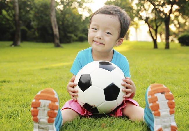 Little boy happily holding a soccer ball, sitting in a field