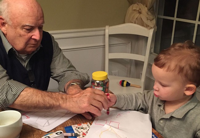 Reminiscent of the old days, a grandfather helps his grandson color while babysitting him