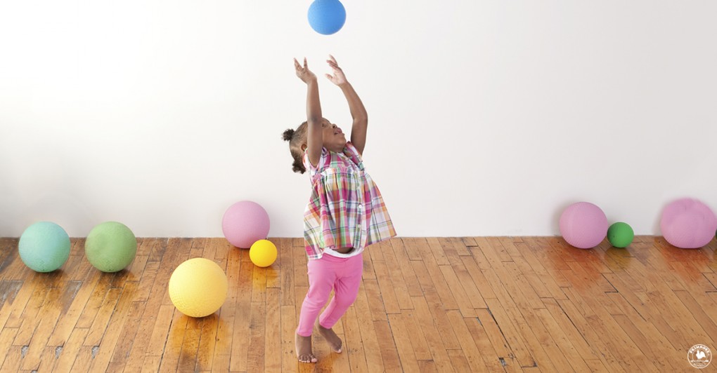 A little girl throws up a ball in the air in a playroom