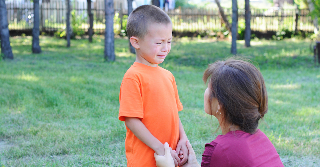 Mother holds hands and calms down crying toddler outside