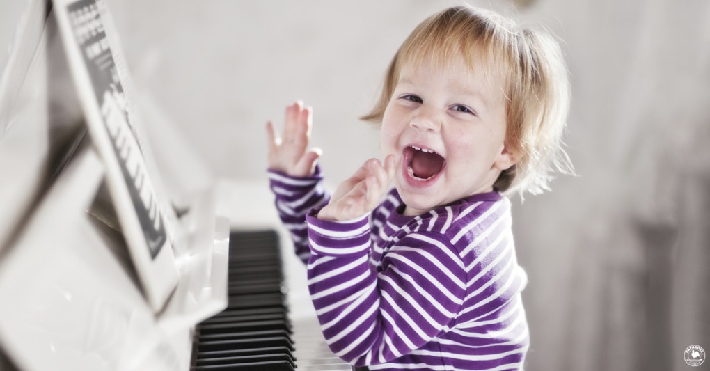 A young child laughs happily as he sits by the piano