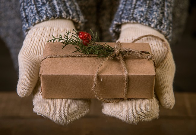 Close up of a little child's hands, wearing mittens and holding a simple and beautifully wrapped Christmas present