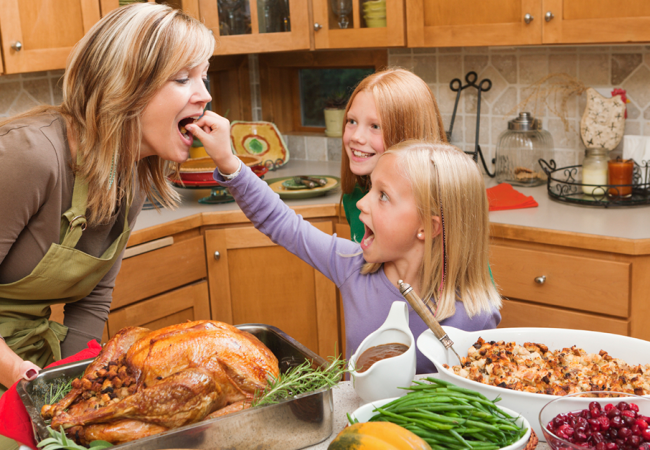 Little girl excitedly offers her mother a bite of their thanksgiving meal as her older sister looks on