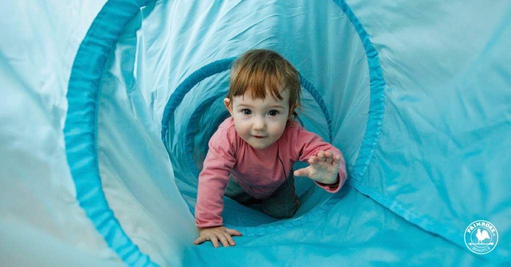 Little girl playing in a tunnel tube, crawling through it and having fun
