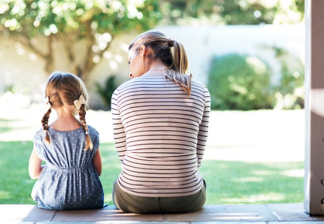 Woman and daughter sit on porch in backyard and have discussion