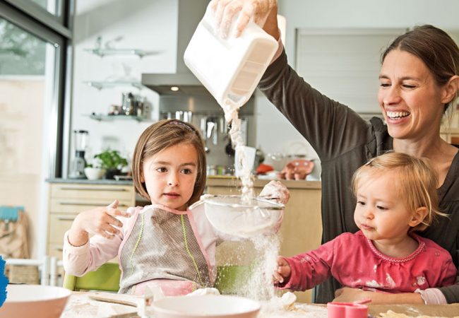 Little girl holds a sieve as her mother pours flour through it