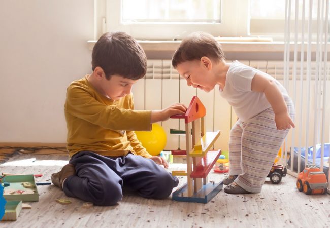 Little boy plays with blocks as his baby brother curiously observes him