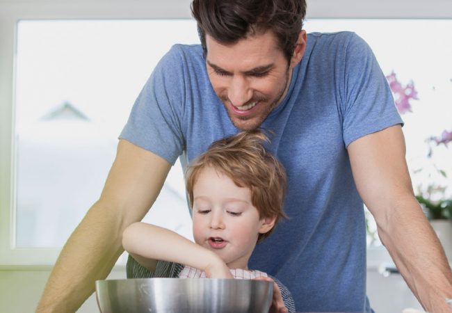 A young boy making cloud dough as his father looks on