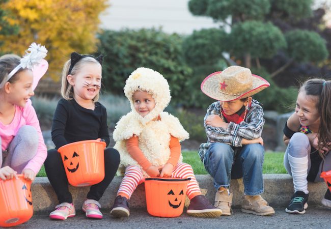 Toddlers in simple Halloween costumes sitting outside