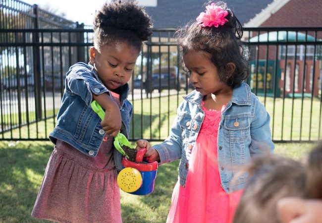 Two Primrose students help each other while playing together in garden