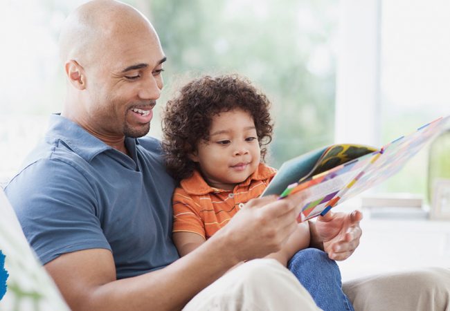 Father happily reads a story book to his young son