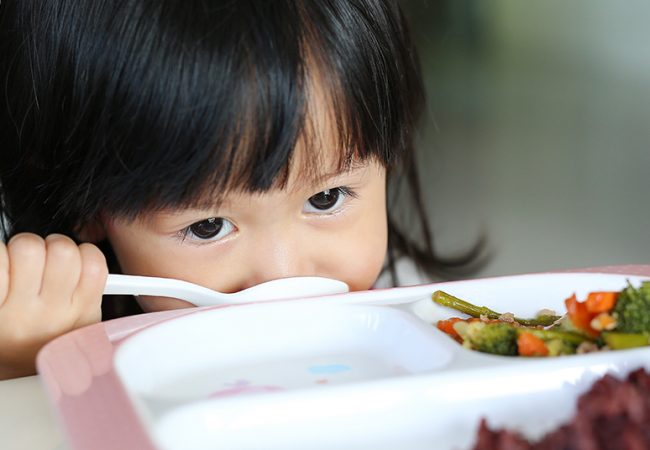 Young girl eyeing her vegetables