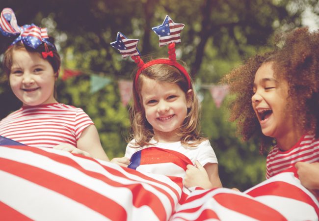 A group of young children playing on the fourth of July with an American flag