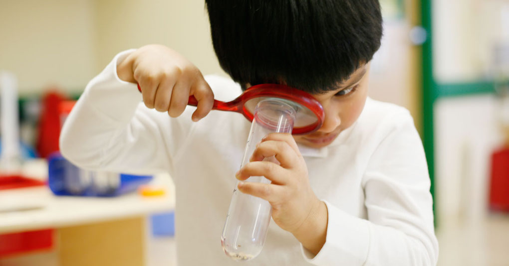 A curious child looks at a solution in a test tube through a magnifying glass