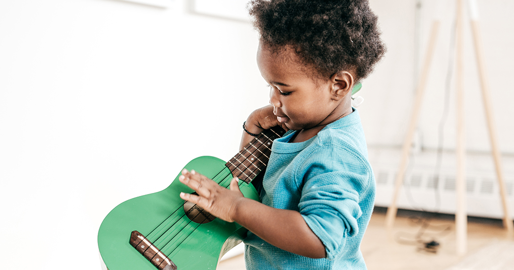 Toddler plays with a green guitar as part of his early musical development.