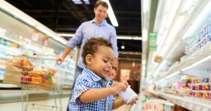 Little boy taking yogurt while shopping with father