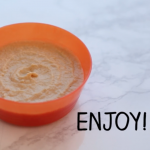 An orange bowl containing hummus