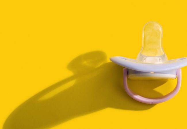 Baby pacifier over a plain yellow background
