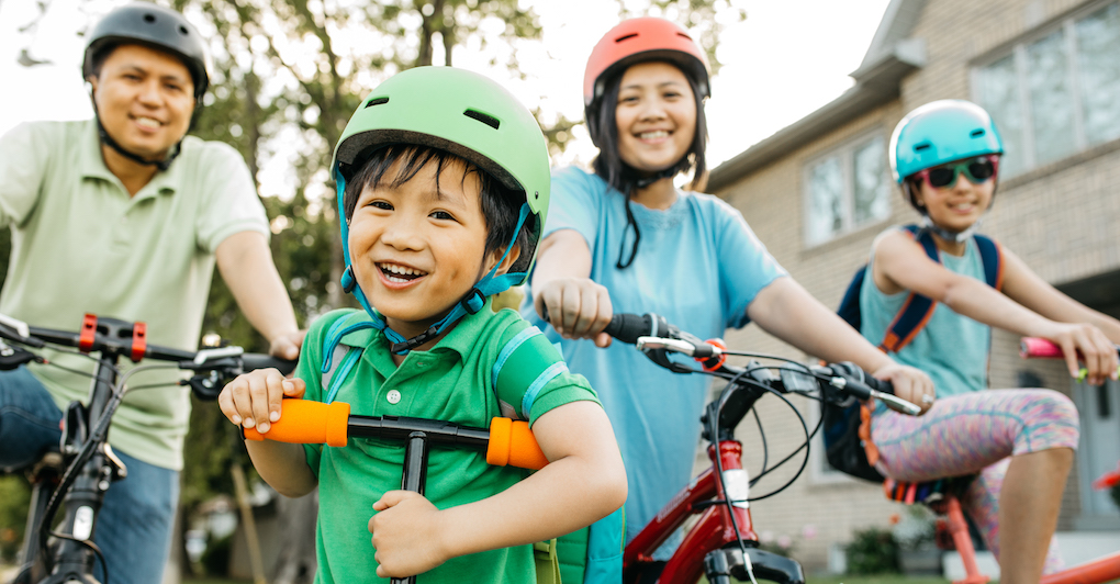 Family of four smiling riding bikes and wearing helmets