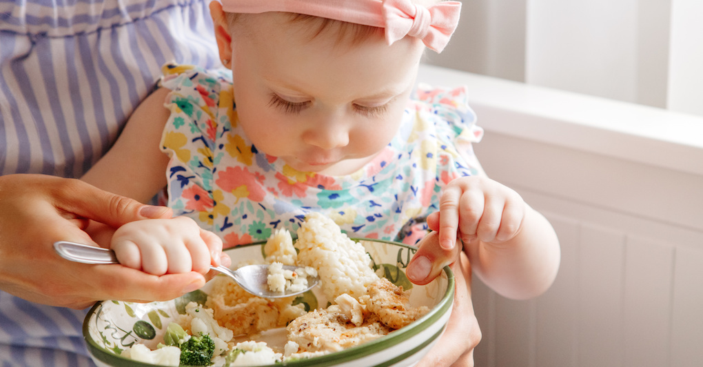Little baby girl eating vegetables and cauliflower off of plate