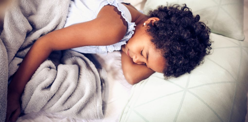 Young girl sleeping on white bed sheets with blanket