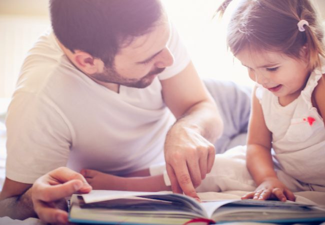 Father teaches daughter Spanish reading bilingual book together in bed