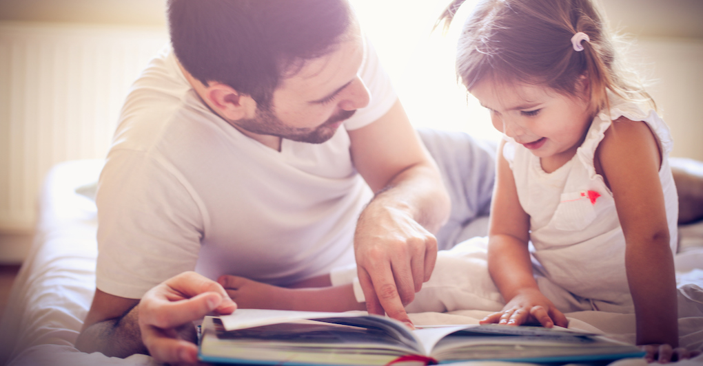 Father teaches daughter Spanish reading bilingual book together in bed