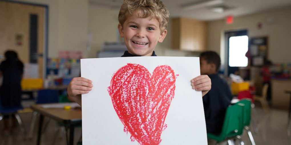 Primrose student smiles and holds white poster with red heart drawn on it