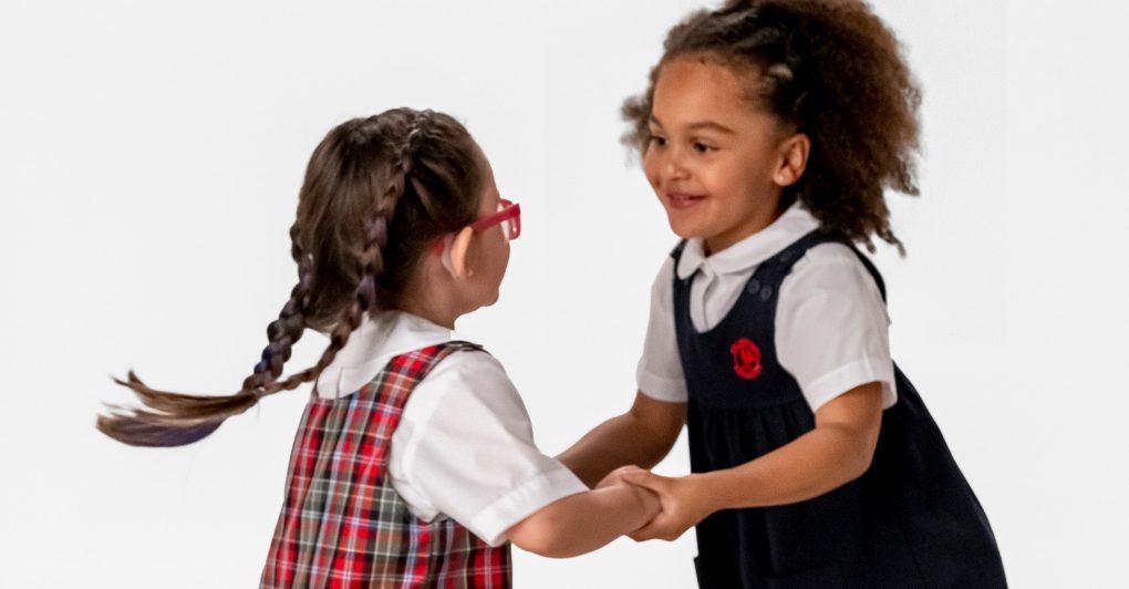 two little girls holding hands and dancing with one another, in their Primrose school uniforms.