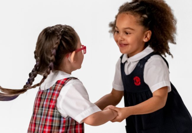 two little girls holding hands and dancing with one another, in their Primrose school uniforms.