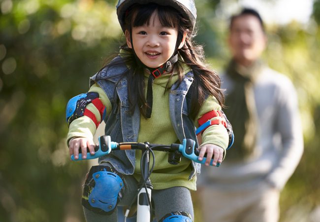 Girl riding bicycle with parent encouraging in the background