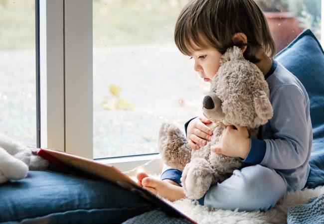 young boy reads in comfort corner and comforts a teddy bear