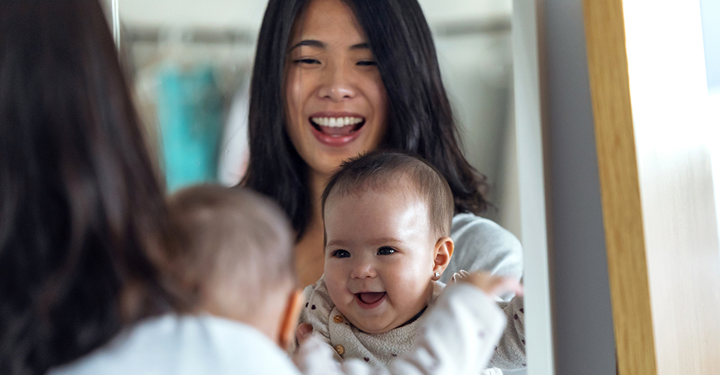woman holding baby both smiling into a mirror