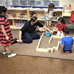chldren and teacher on the floor in a classroom helping a robot navigate a maze