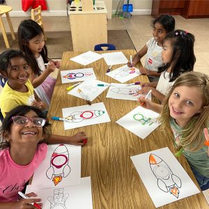 children in a classroom at a table coloring rocket ships